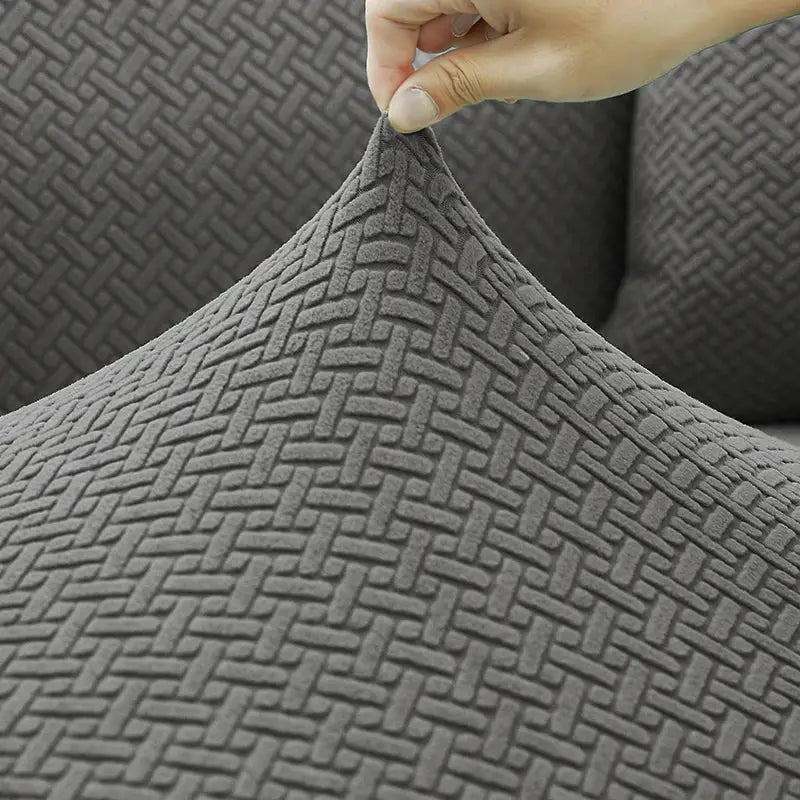 Elastic jacquard sofa cover in gray fabric with a woven pattern, being stretched at a corner.