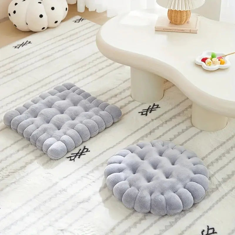 Large biscuit-shaped plush cushion and round gray tatami-back pillow on a striped rug.