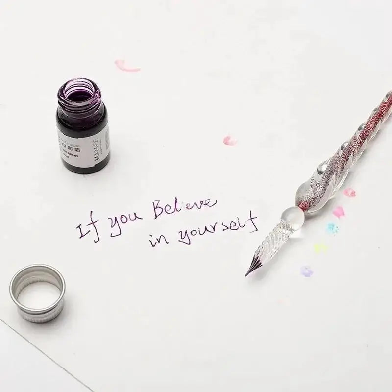 Crystal glass dipping pen with jeweled handle beside purple ink bottle on white surface.