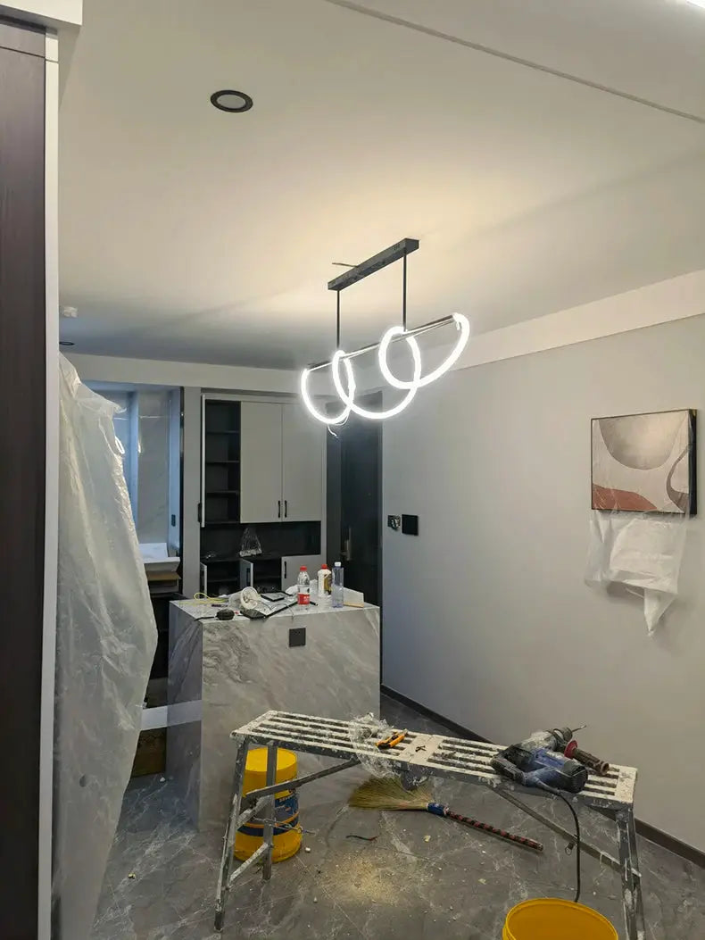 Pendant chandelier with three white circular LED rings hanging over a marble kitchen island.