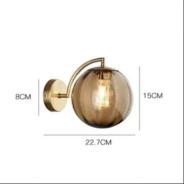 Modern LED wall lamp sconce with amber glass globe and brass finish, 22.7cm wide by 15cm tall.