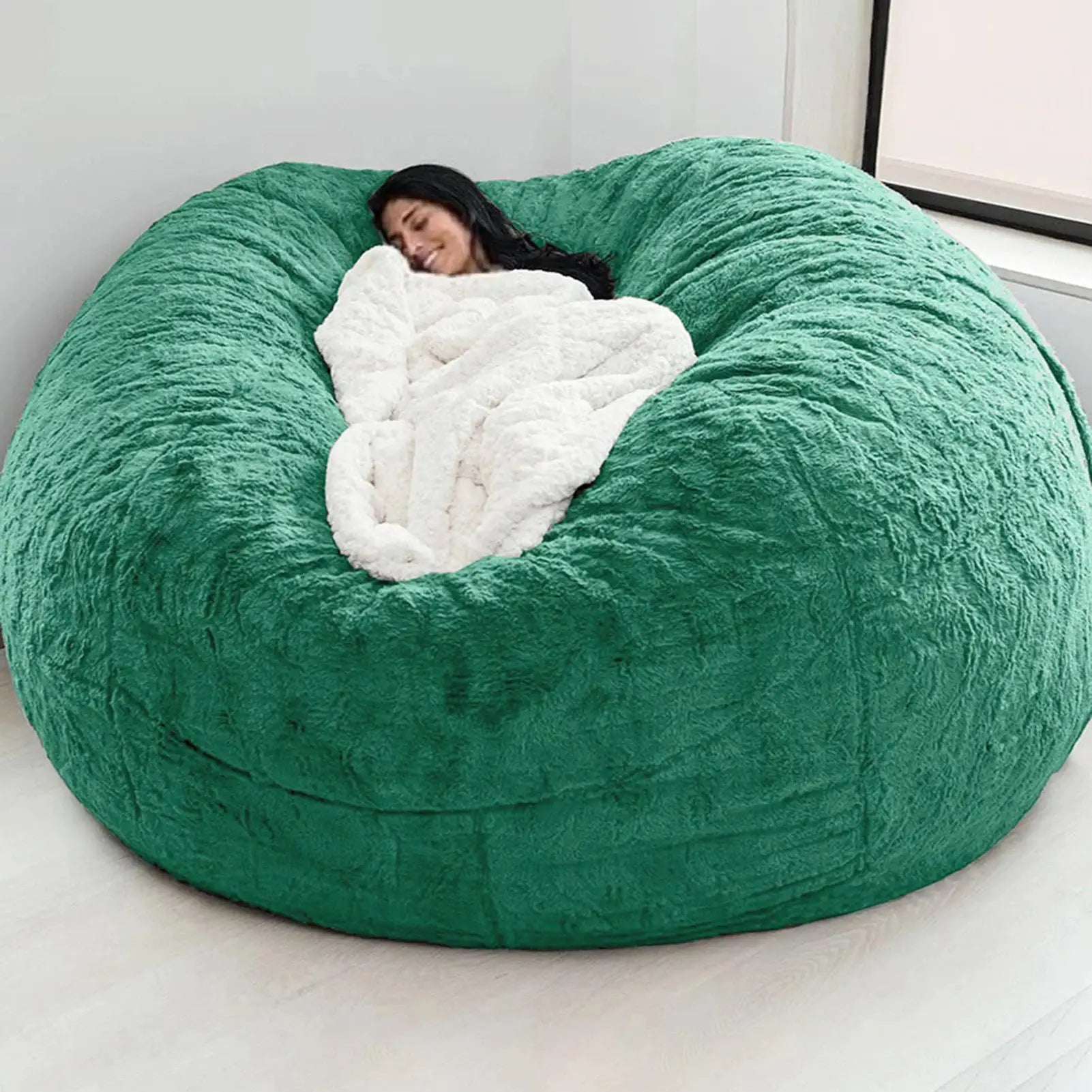 Bean bag sofa bed in green plush fabric with white fluffy blanket and a person lounging inside