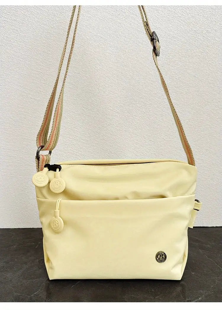 Simples Market ivory nylon crossbody bag with adjustable striped strap, front pocket, and zipper closure.