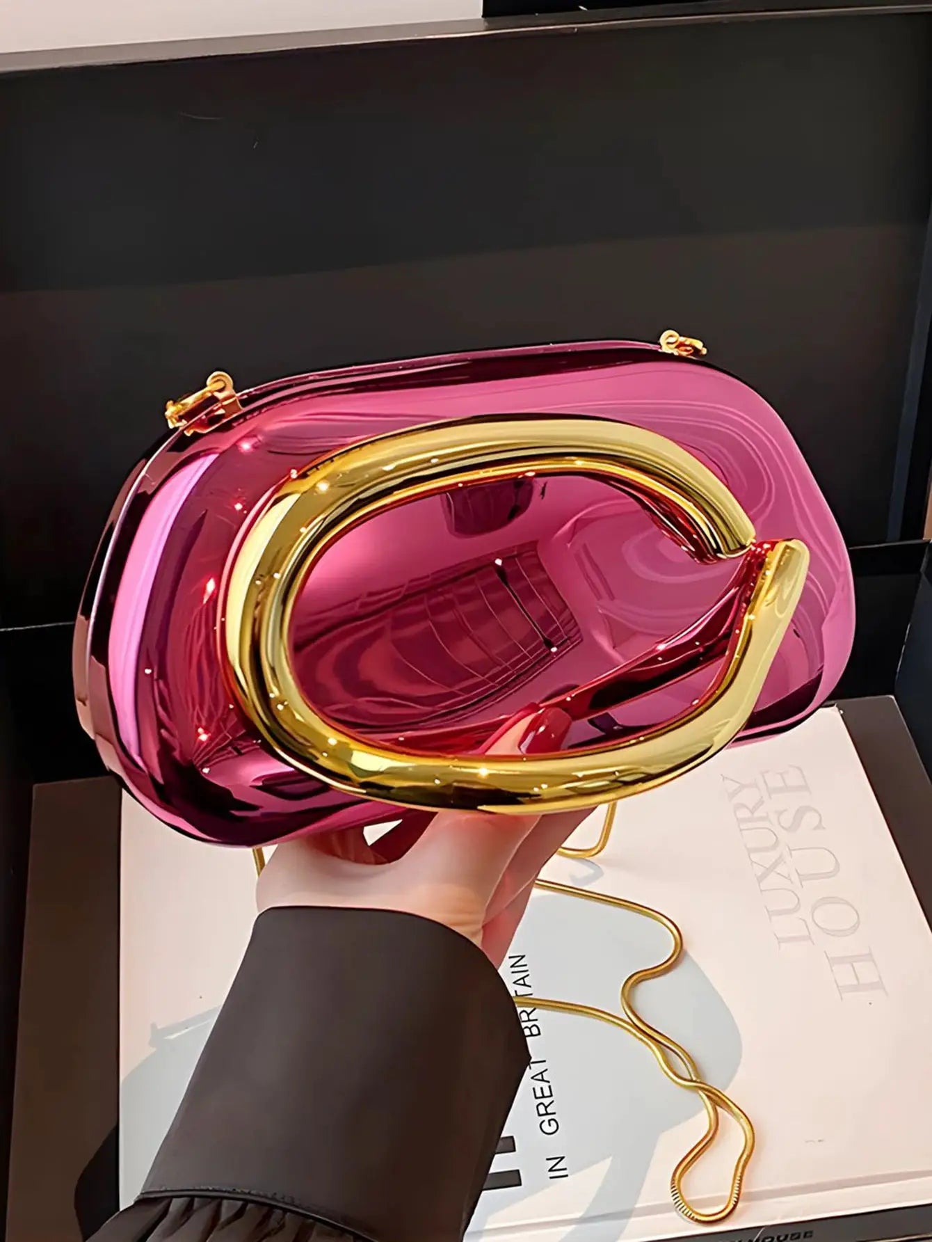 Pink acrylic box crossbody bag with gold-tone curved handle and gold chain strap.