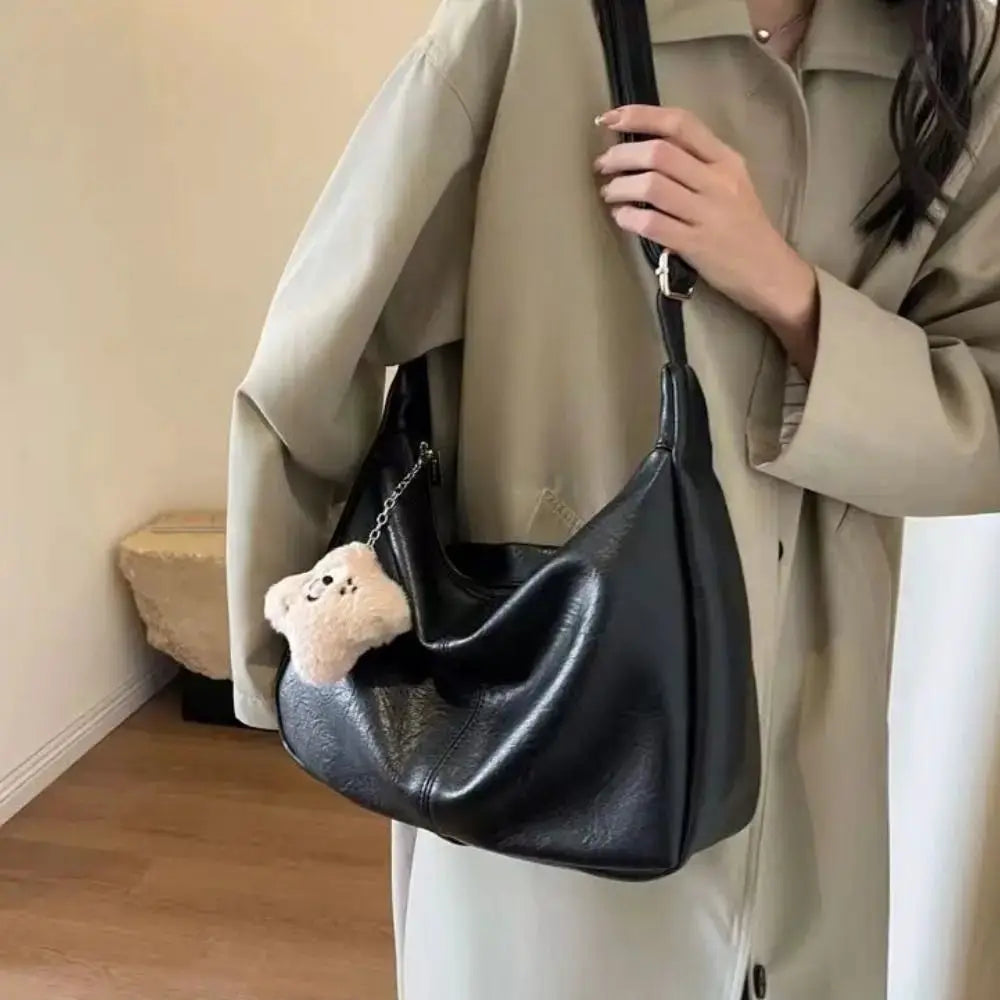 Trendy slouchy women's shoulder bag in black PU leather with teddy bear keychain, large-capacity hobo tote.