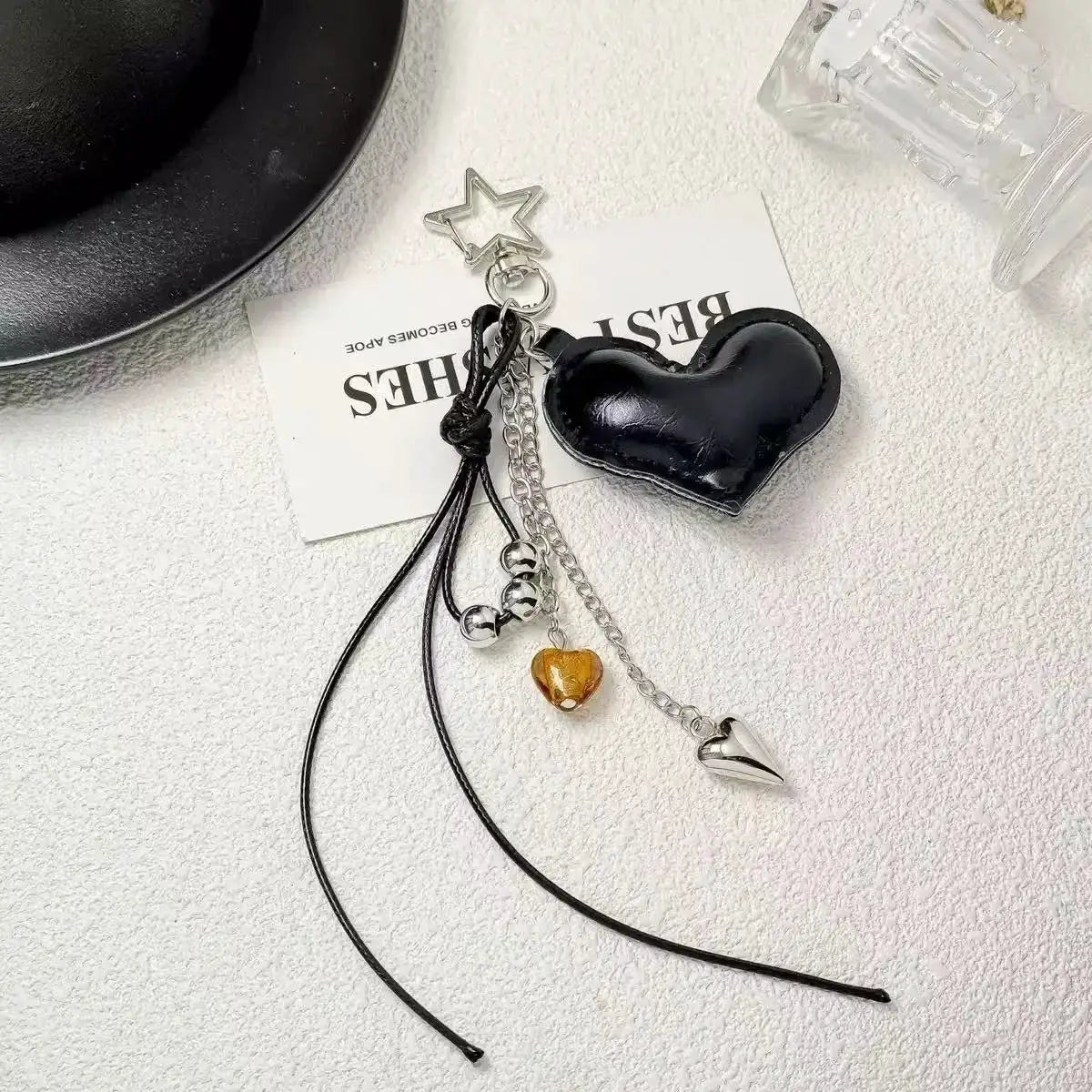 Black heart-shaped leather bag charm with silver chain, star charm, amber bead and leather cords.