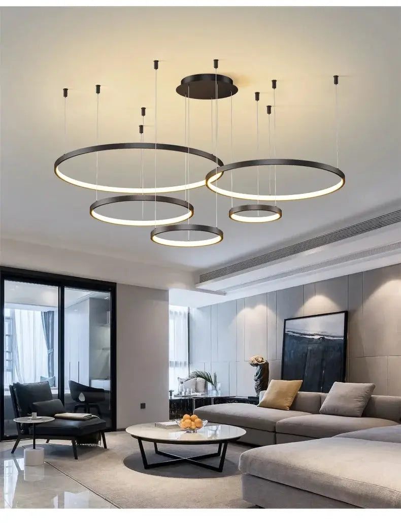 Minimalist ring pendant lights; set of circular black metal LED rings over a modern living room.