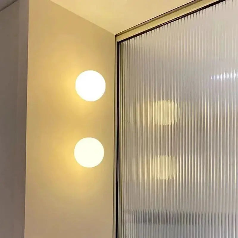 Milky white glass ball wall lamp with frosted round globes beside a frosted glass panel.
