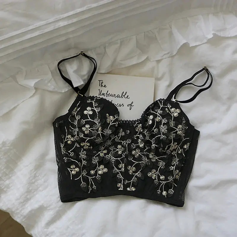 Black lace bralette with silver floral embroidery and adjustable straps on white bedding.