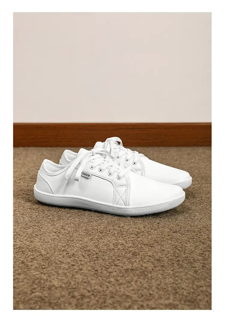 Pair of white lace-up sneakers with flat soles on beige carpet