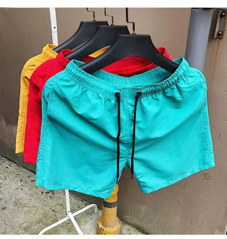 Men's swim shorts on hangers; turquoise pair with black drawstrings in front, red and yellow variants behind