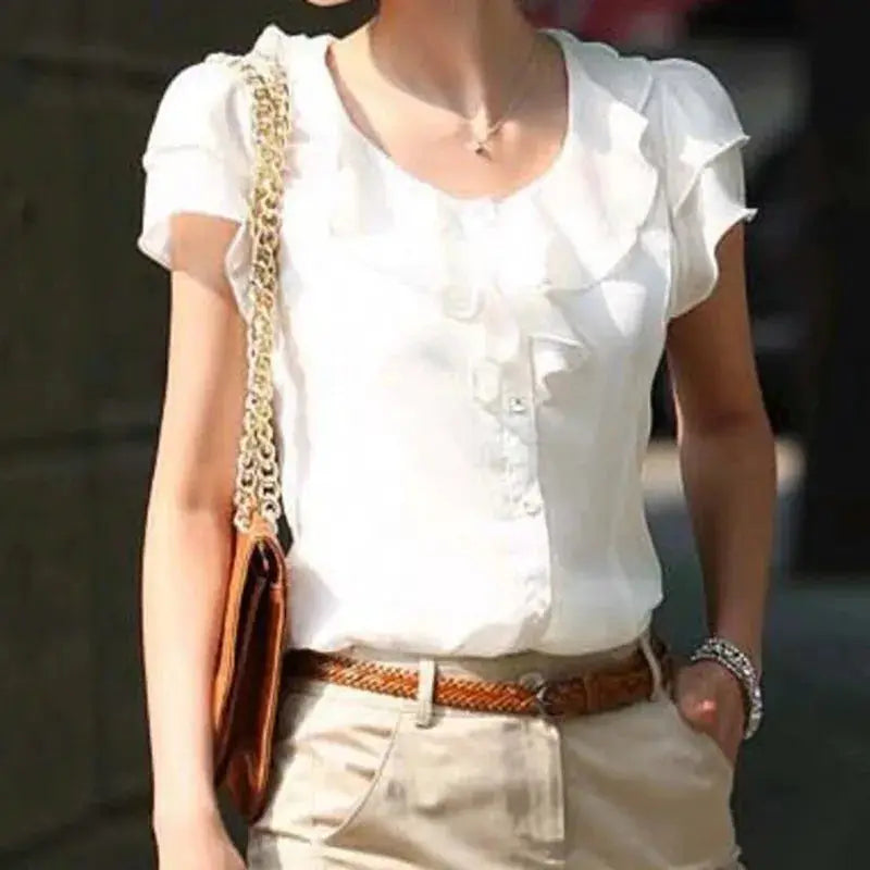 White women's blouse with ruffle front and short puff sleeves, shown with beige trousers and brown woven belt.