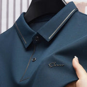 Men's polo shirt in navy blue with textured fabric and small metal logo on chest; business casual golf style.