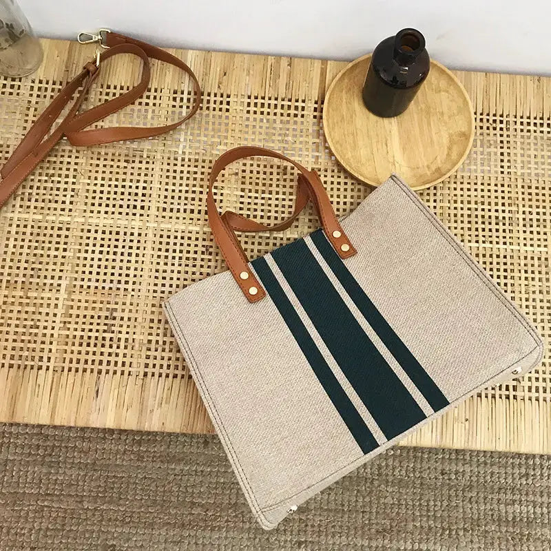 Canvas stripe tote bag with brown leather handles and long strap; beige with dark green center stripe and light side stripes.
