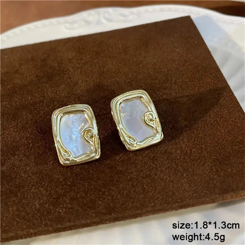Pair of rectangular gold-tone earrings with iridescent mother-of-pearl centers and decorative gold swirls.