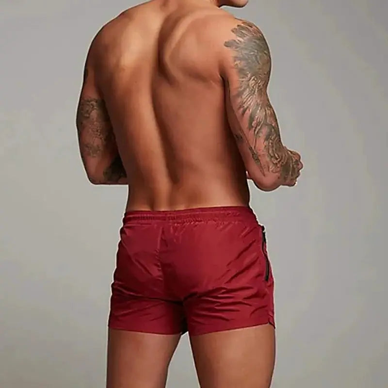 Men's red swimming trunks by Simples Market, back view on a tattooed model.