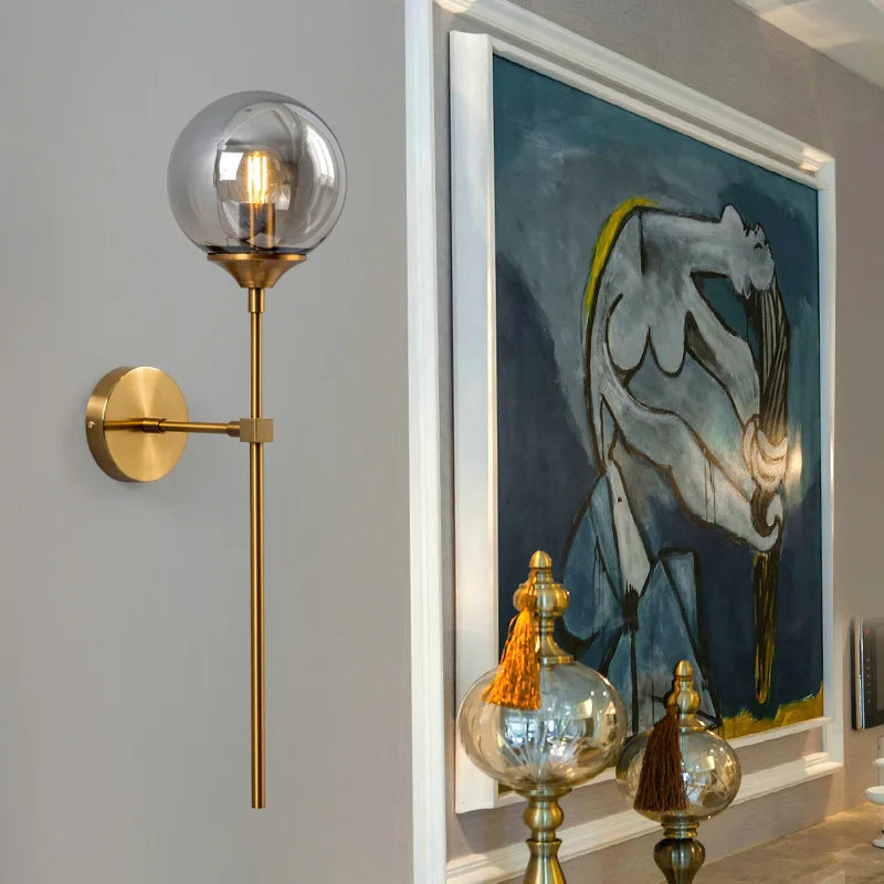 Modern glass ball wall lamp sconce in brass finish with clear globe shade and visible Edison bulb; wall-mounted.