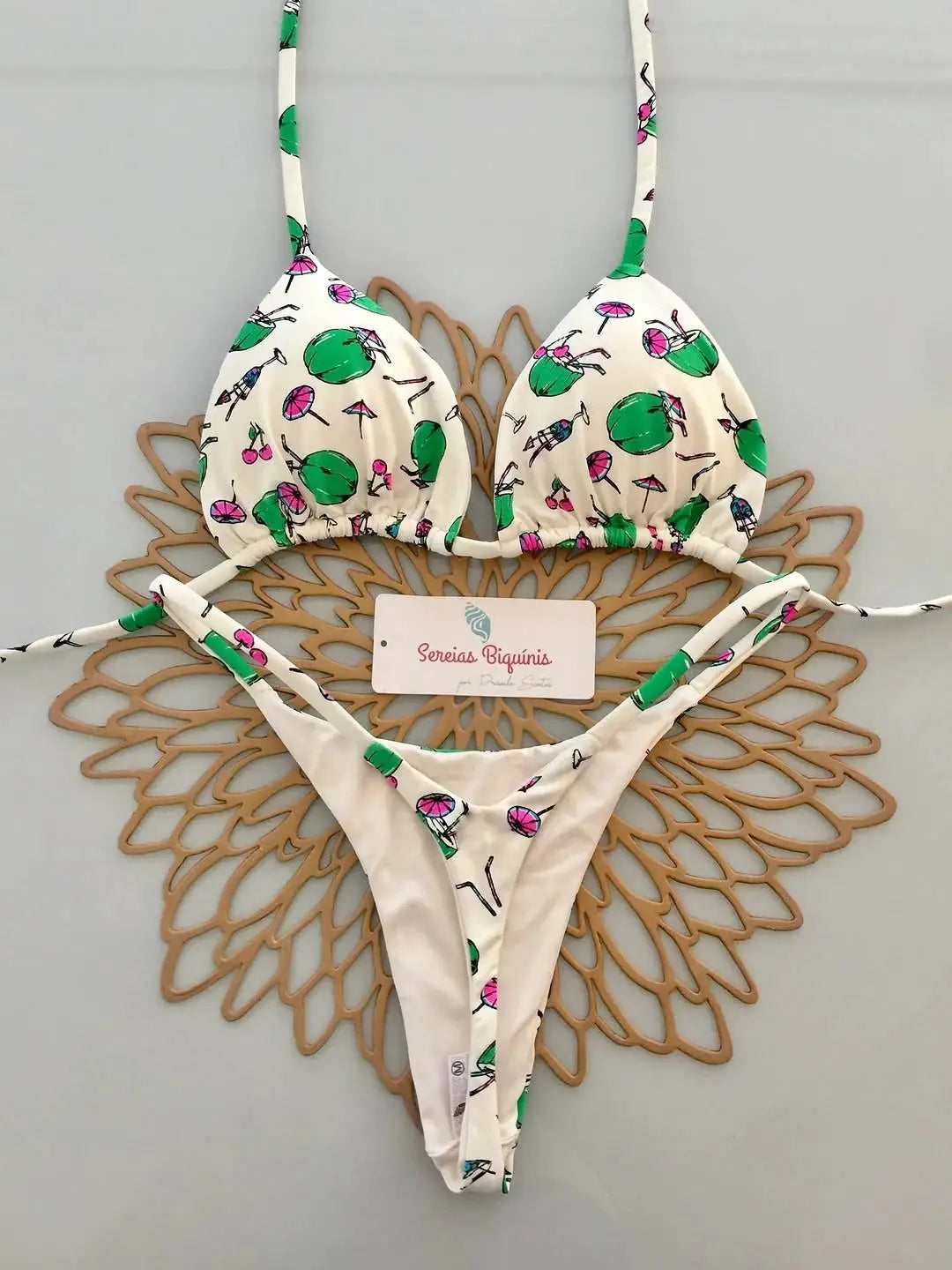 Two-piece micro bikini set in white tropical print with green accents, halter top and thong bottom.