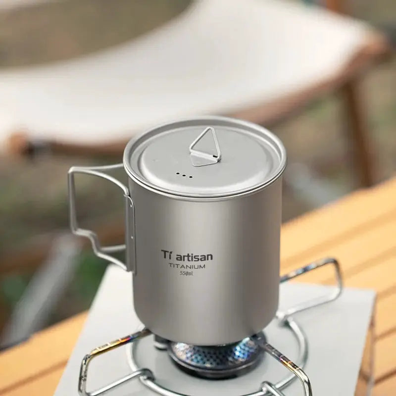 Tiartisan titanium camping mug with folding handle and lid, 550ml, shown on a camping stove