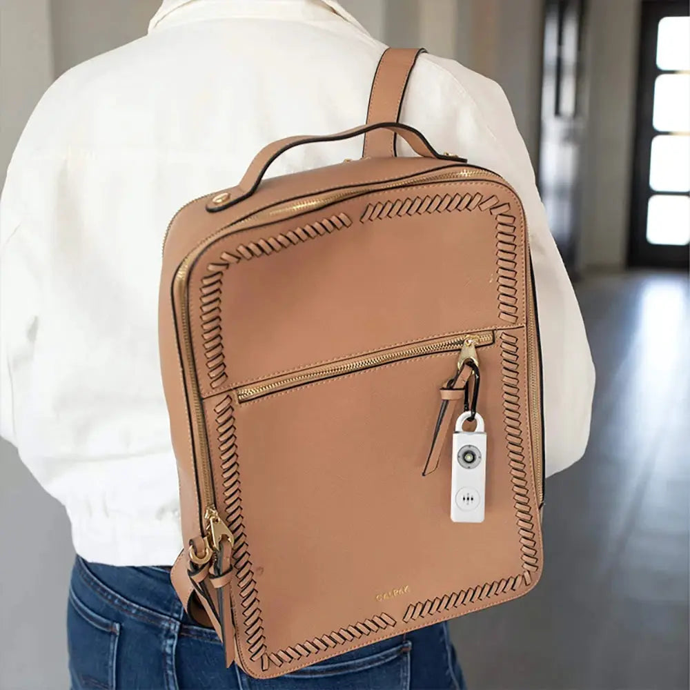 130dB rechargeable personal alarm keychain with LED light attached to tan backpack zipper