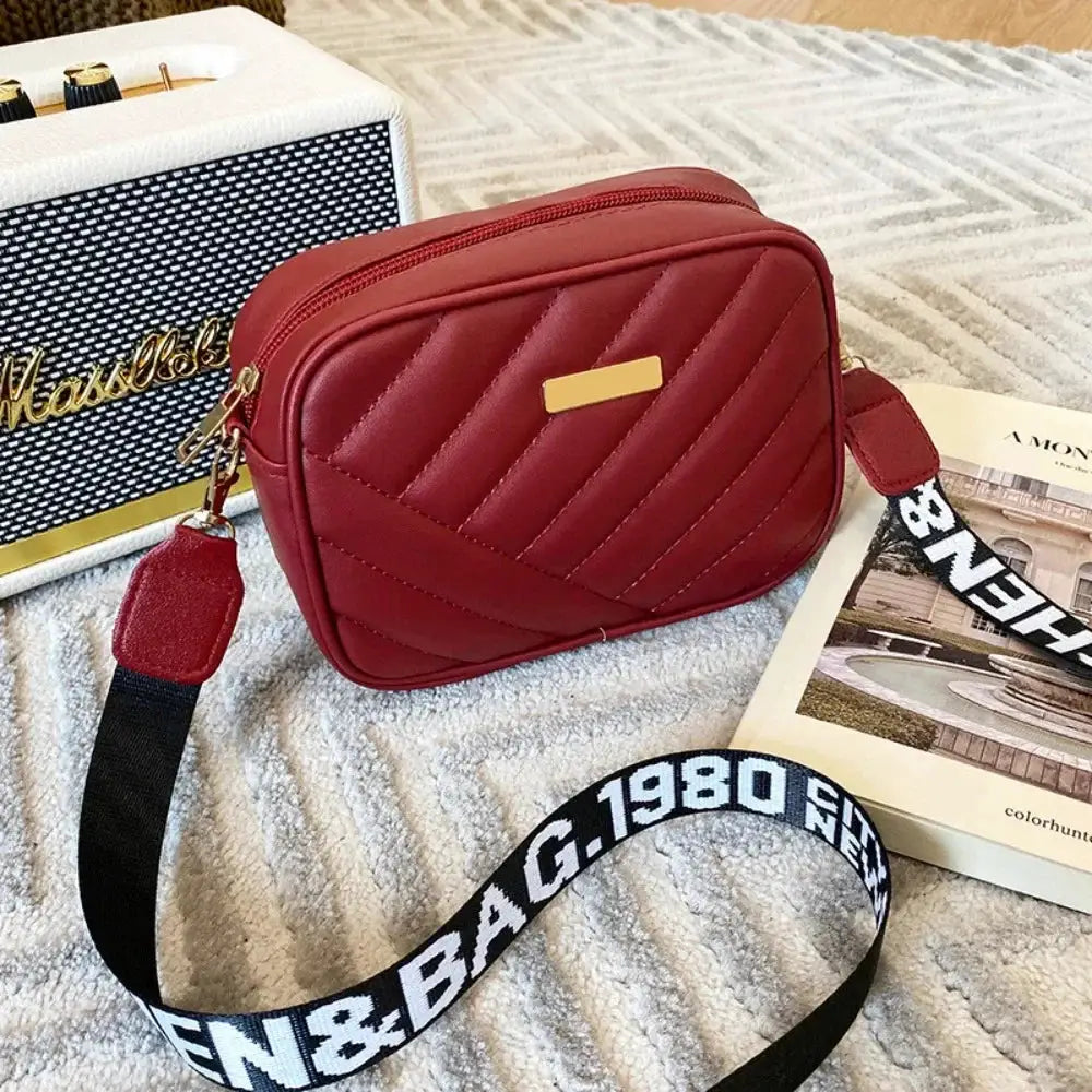 Red PU leather shoulder bag with diagonal quilted pattern, gold plaque, and detachable black-and-white strap.