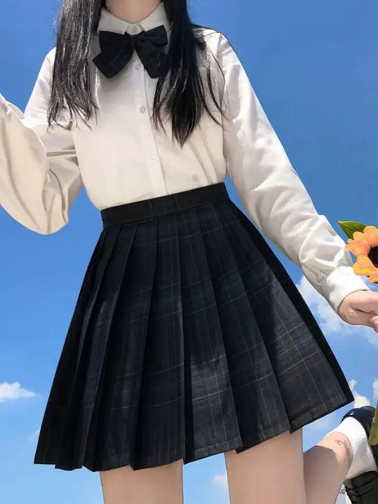 ZOKI plaid pleated high-waisted skirt in dark plaid, paired with a white blouse and black bow.