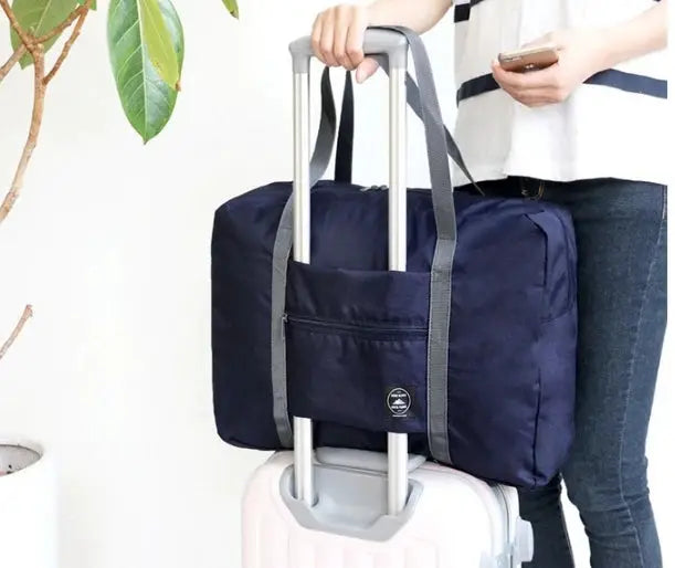 Large-capacity travel bag by Simples Market in navy with gray handles, strapped to a rolling suitcase