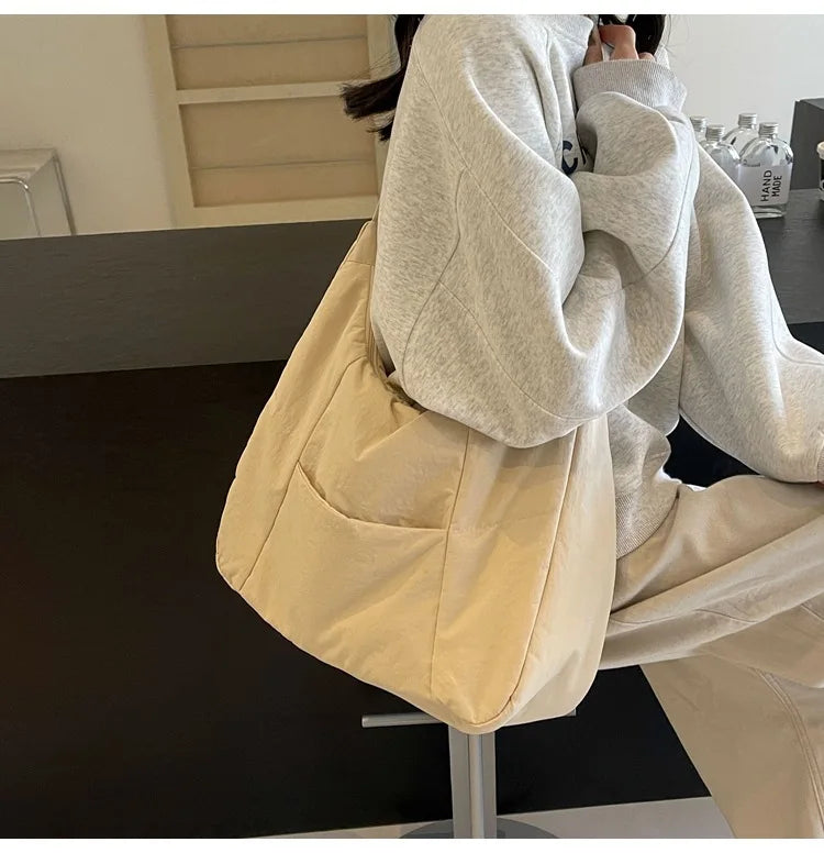 Shoulder bag in beige soft-cloth with front pockets, worn with a gray hoodie