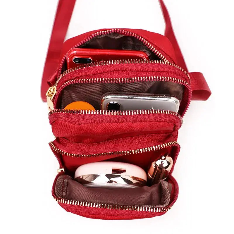 Red waterproof crossbody bag with multiple zip compartments, holding two phones and cosmetics
