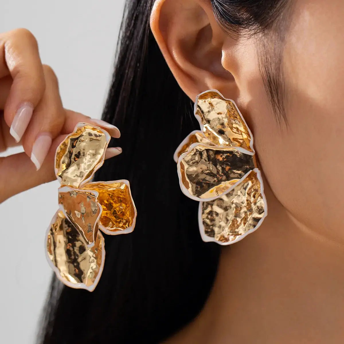 Pair of metal irregular pleated petal earrings by Simples Market, gold hammered petals with white edges.