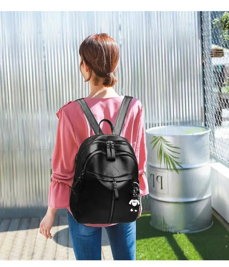 Black leather backpack with bear charm worn by a woman in a pink top outdoors