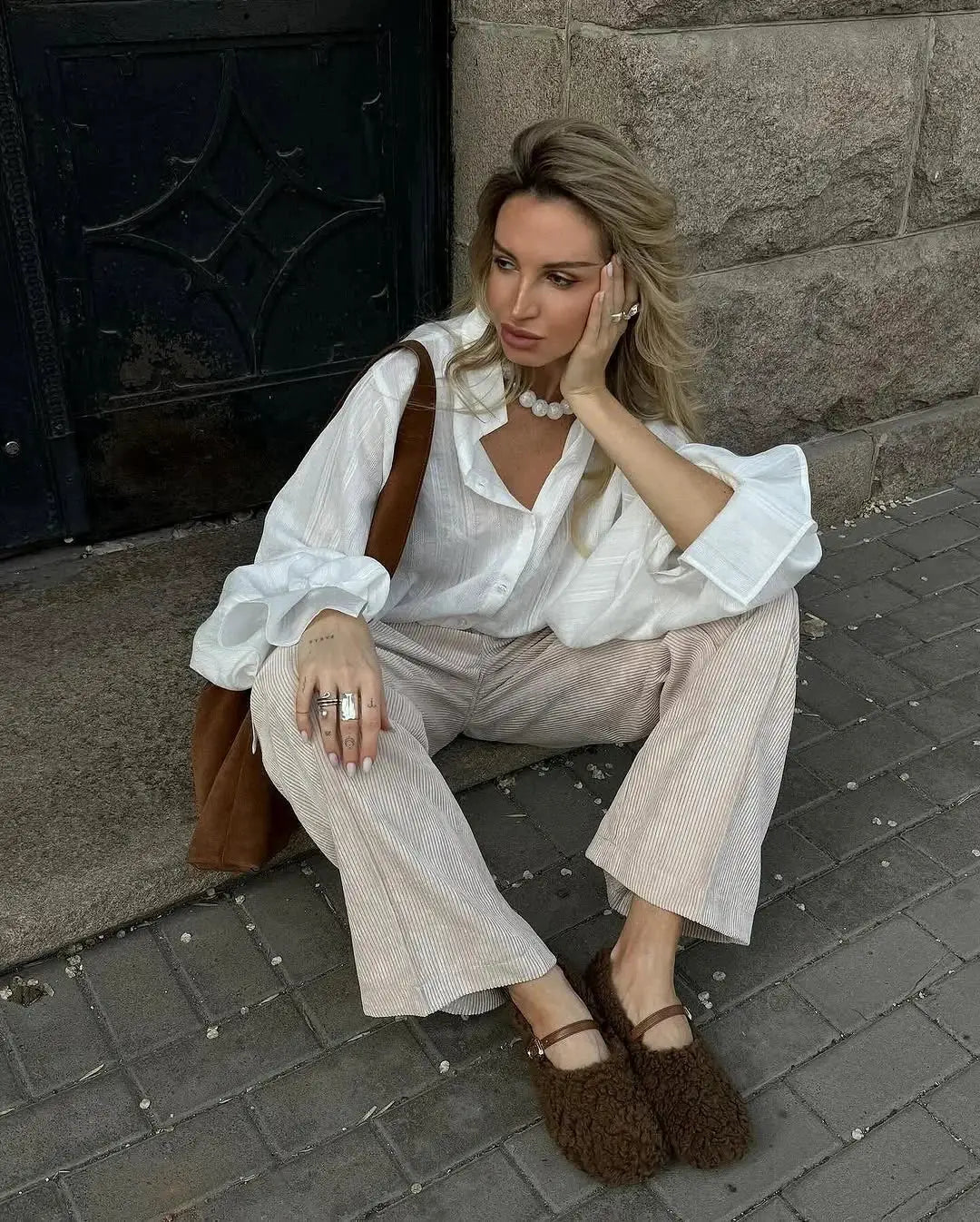 Oversize white cotton button-up shirt worn by a woman, paired with light striped wide-leg pants and brown accessories.