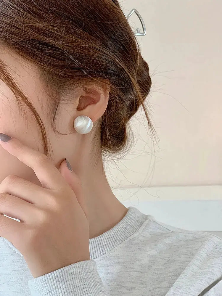 Pearl stud earrings with frosted white finish worn on the ear