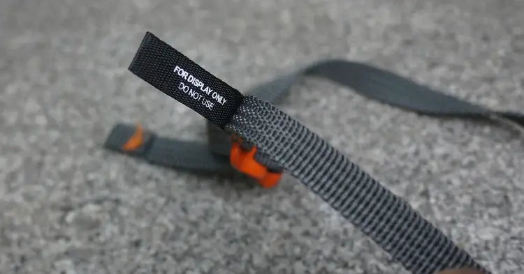 Luggage strap with gray woven webbing and orange quick-release buckle.