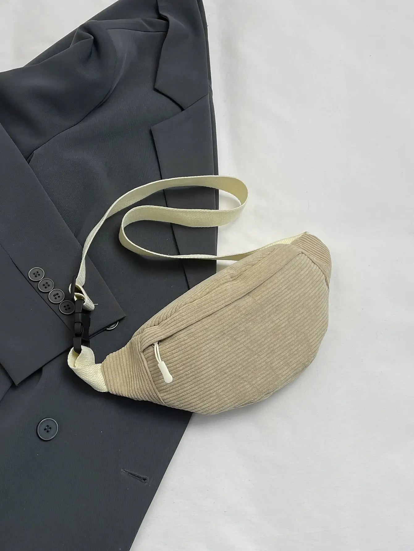 Beige corduroy fanny pack with white zipper, worn over a dark blazer.