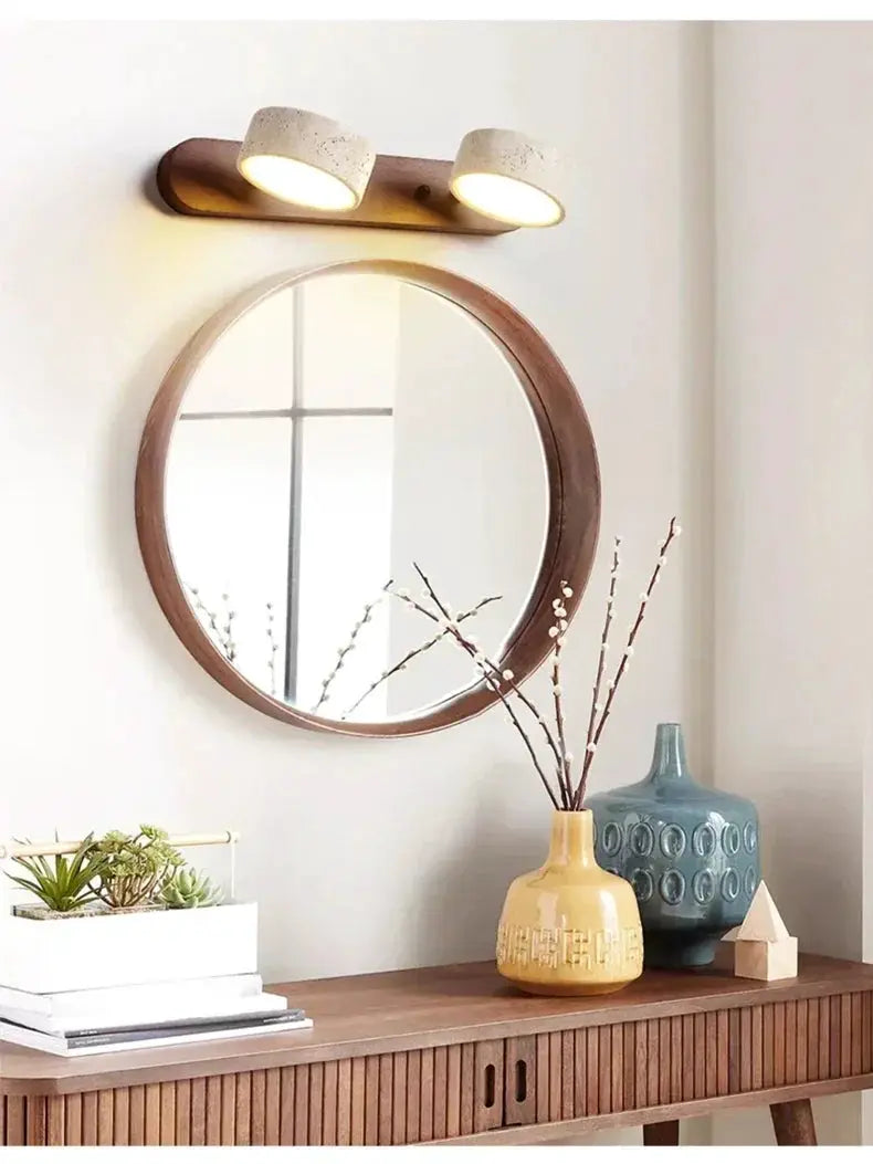 Round LED wall light by Simples Market with concrete-style cylinders on a wood mount above a round wood-framed mirror