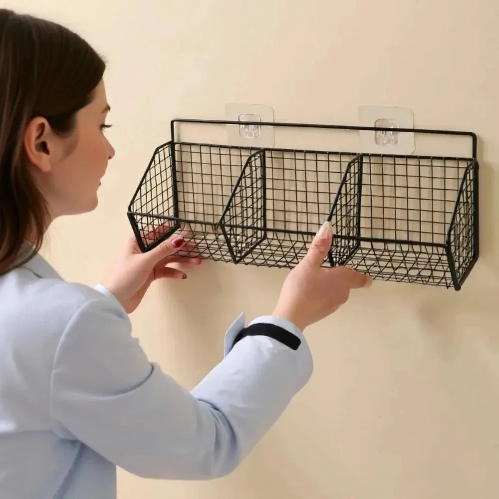Wall-mounted metal wire storage basket with three compartments for spices, garlic, onions, and vegetables.