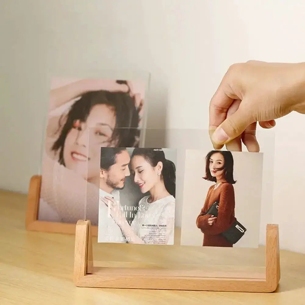 Photo frame by Simples Market: U-shaped transparent acrylic frame on a light wooden desktop stand displaying multiple pictures.