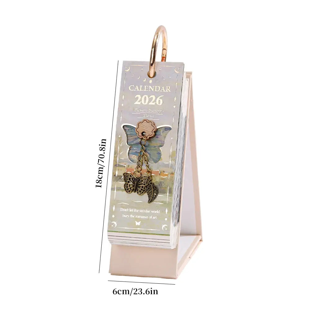 Desk calendar 2026 with gold ring binding and butterfly charm on a beige stand