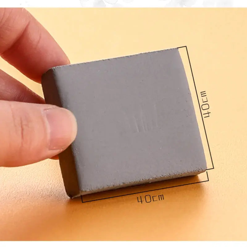 Gray kneaded eraser for drawing, held between fingers on a yellow surface