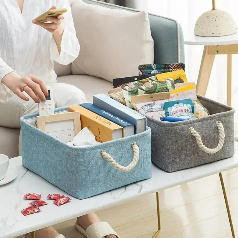 Two folding linen storage baskets with rope handles in blue and gray on a coffee table