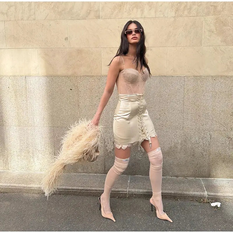 Beige lace-up mini skirt with patchwork and lace trim; paired with nude thigh-high stockings and pointed heels.
