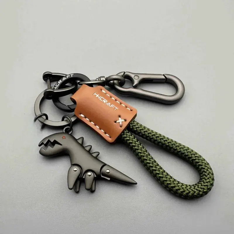 Motorcycle decoration keychain by Simples Market with green braided rope, black metal dinosaur charm and brown leather tag