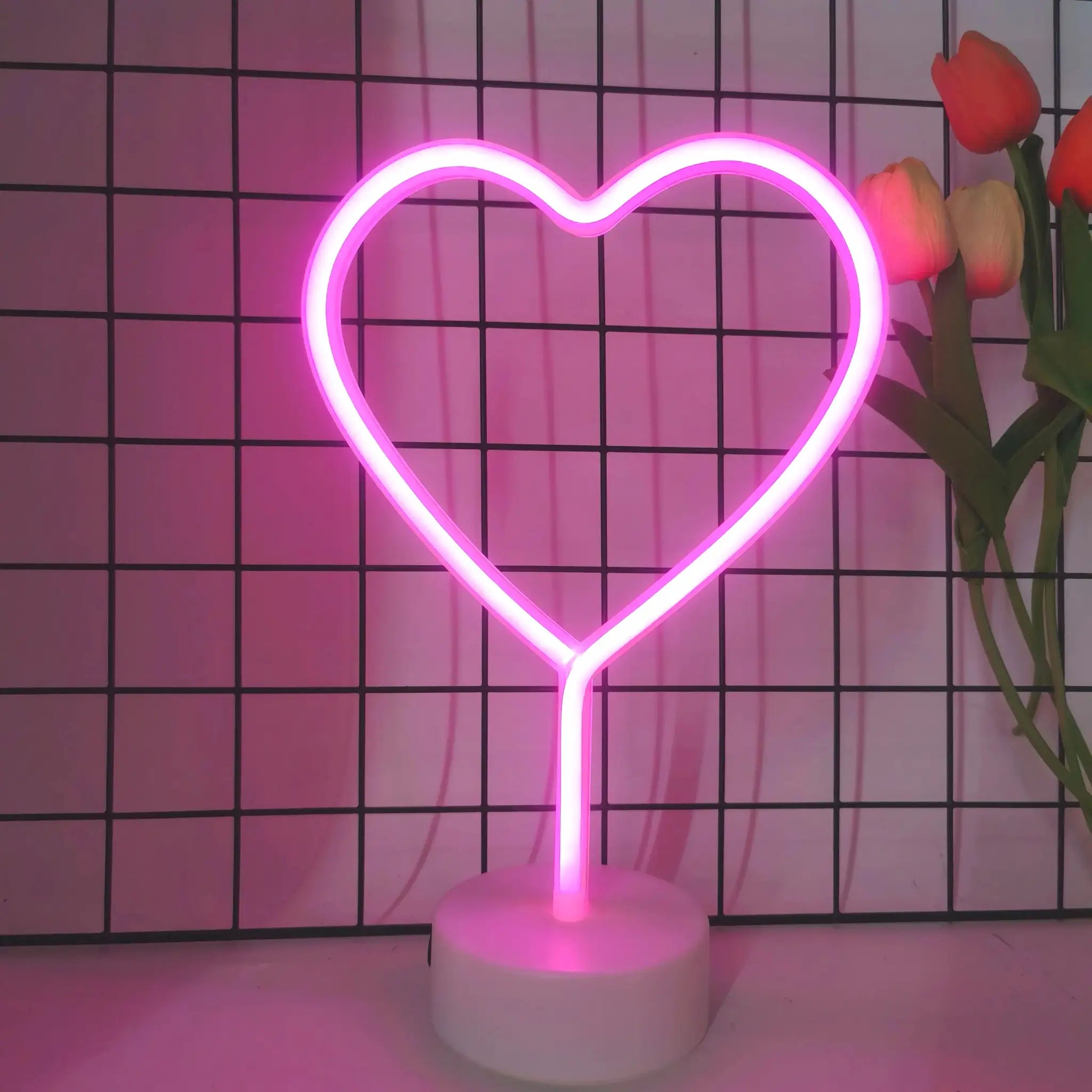 Simples Market heart-shaped neon light on white base, pink glow against grid backdrop with tulips.