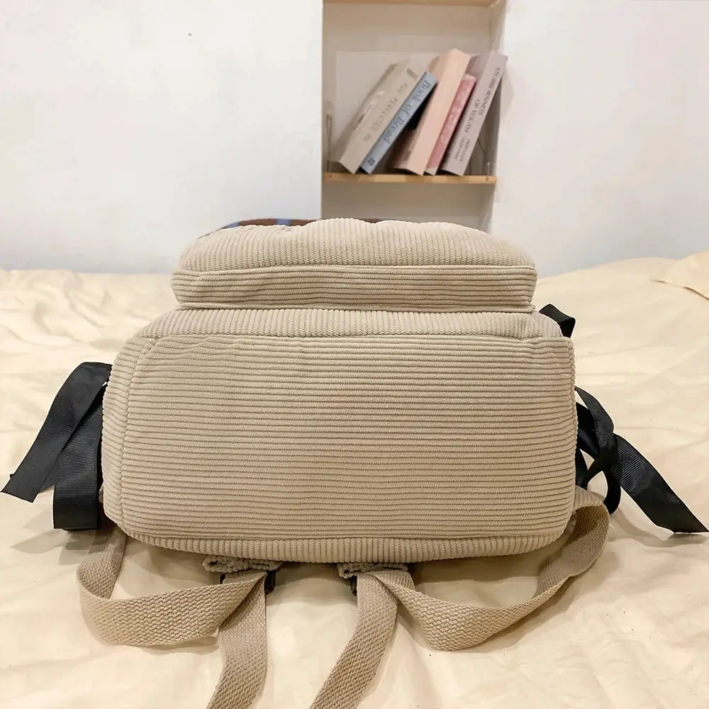 Backpack in beige corduroy with ribbed texture, beige shoulder straps and black side straps.