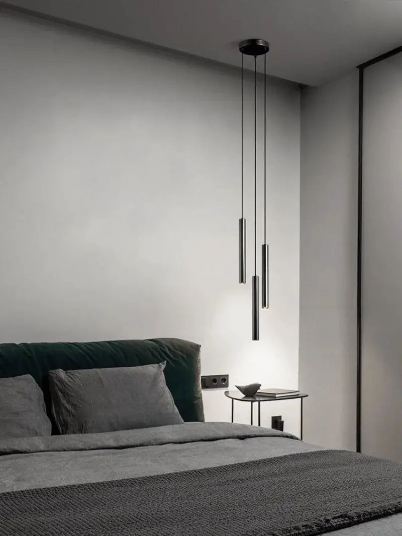 Minimalist bedside pendant lamp set with three black metal cylinder pendants over a bed.