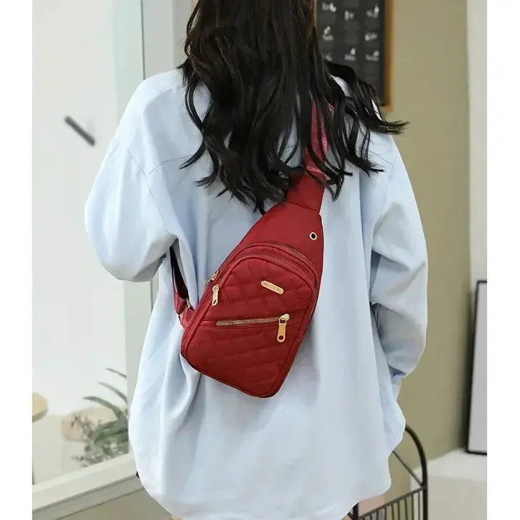 Red quilted composite fabric crossbody bag with gold zippers worn by a woman in a light blue shirt