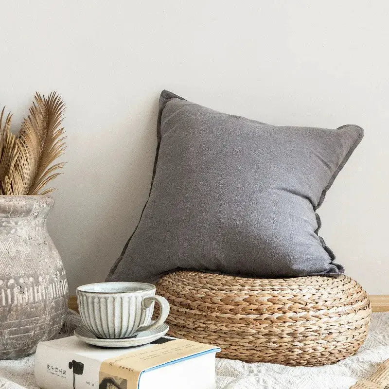 Decorative ramie cushion cover in gray on a woven rattan pouf, boho farmhouse living room decor.