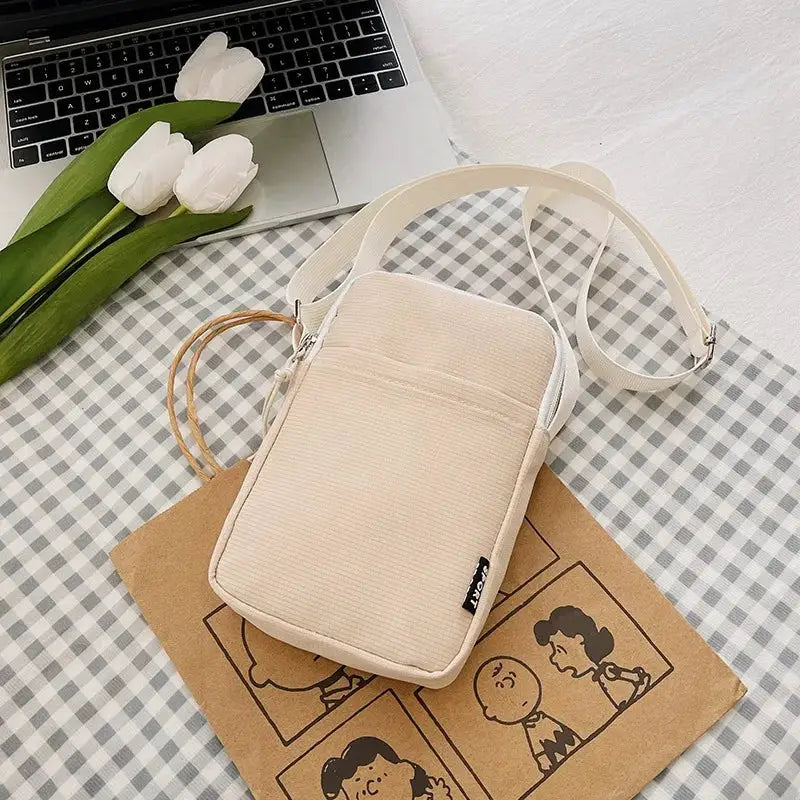 Beige vertical shoulder messenger bag by Simples Market with white strap and front pocket.
