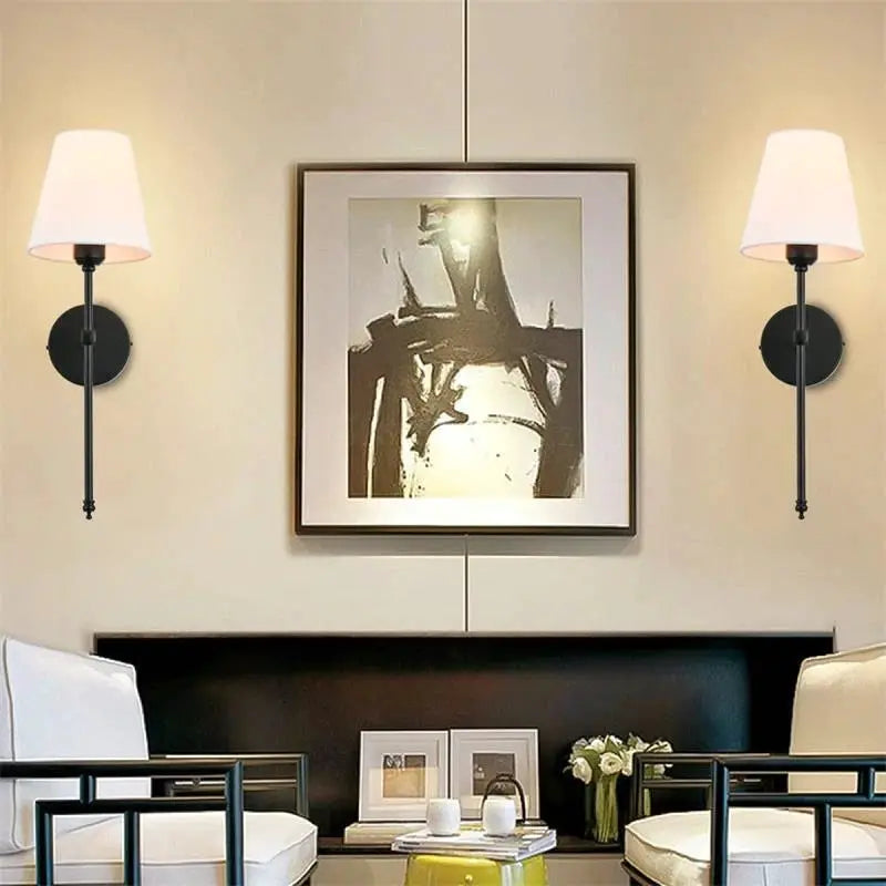 Pair of modern American wall lamps with black metal bodies and white fabric shades beside framed artwork.